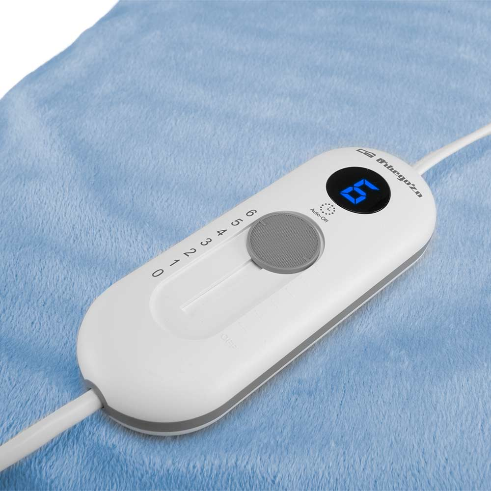 Biały kontroler koca elektrycznego z cyfrowym wyświetlaczem '6'. Leży na niebieskim kocu. Widoczne pokrętło i kabel zasilający.