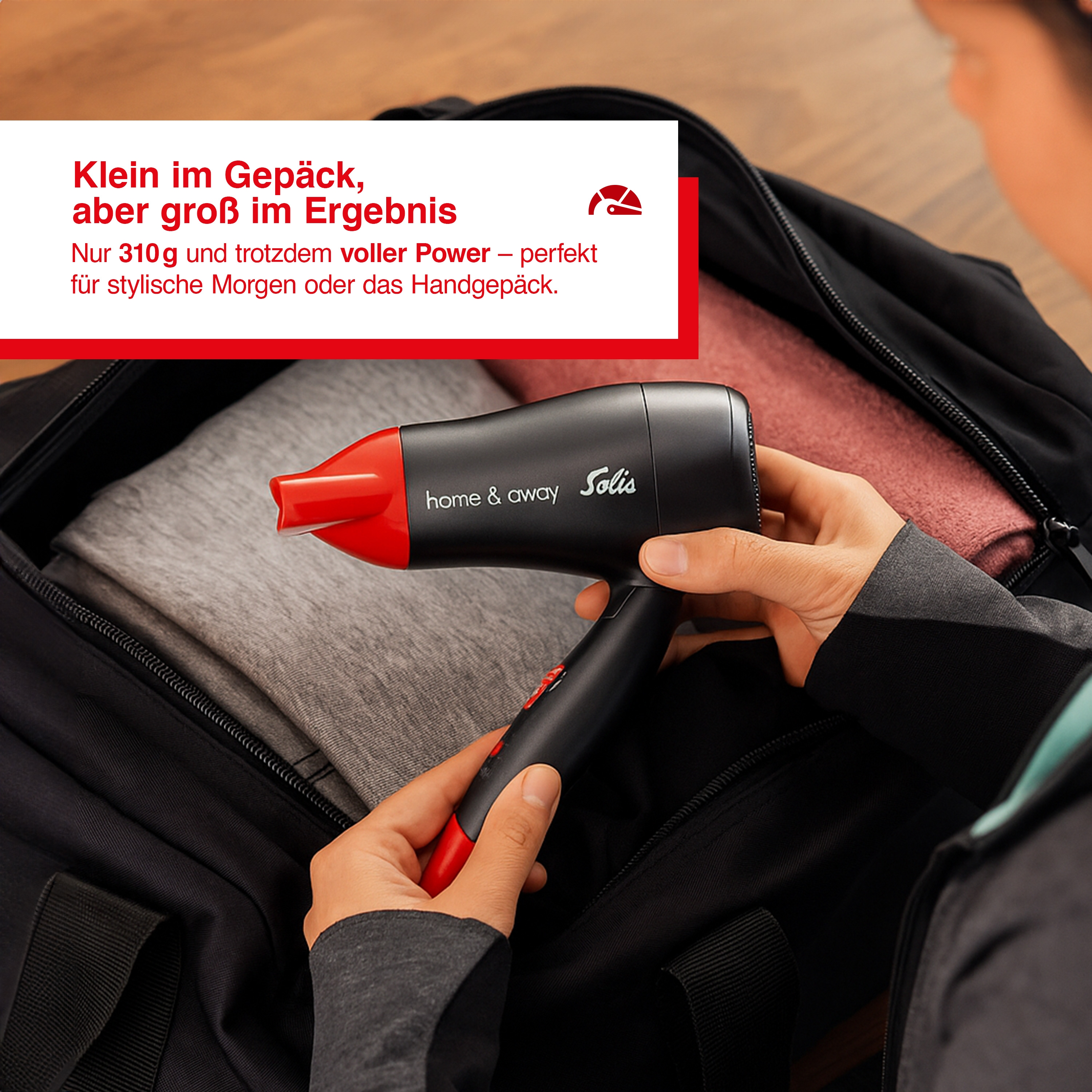 Osoba trzymająca czarno-czerwoną suszarkę do włosów w torbie, z tekstem promującym jej przenośność.