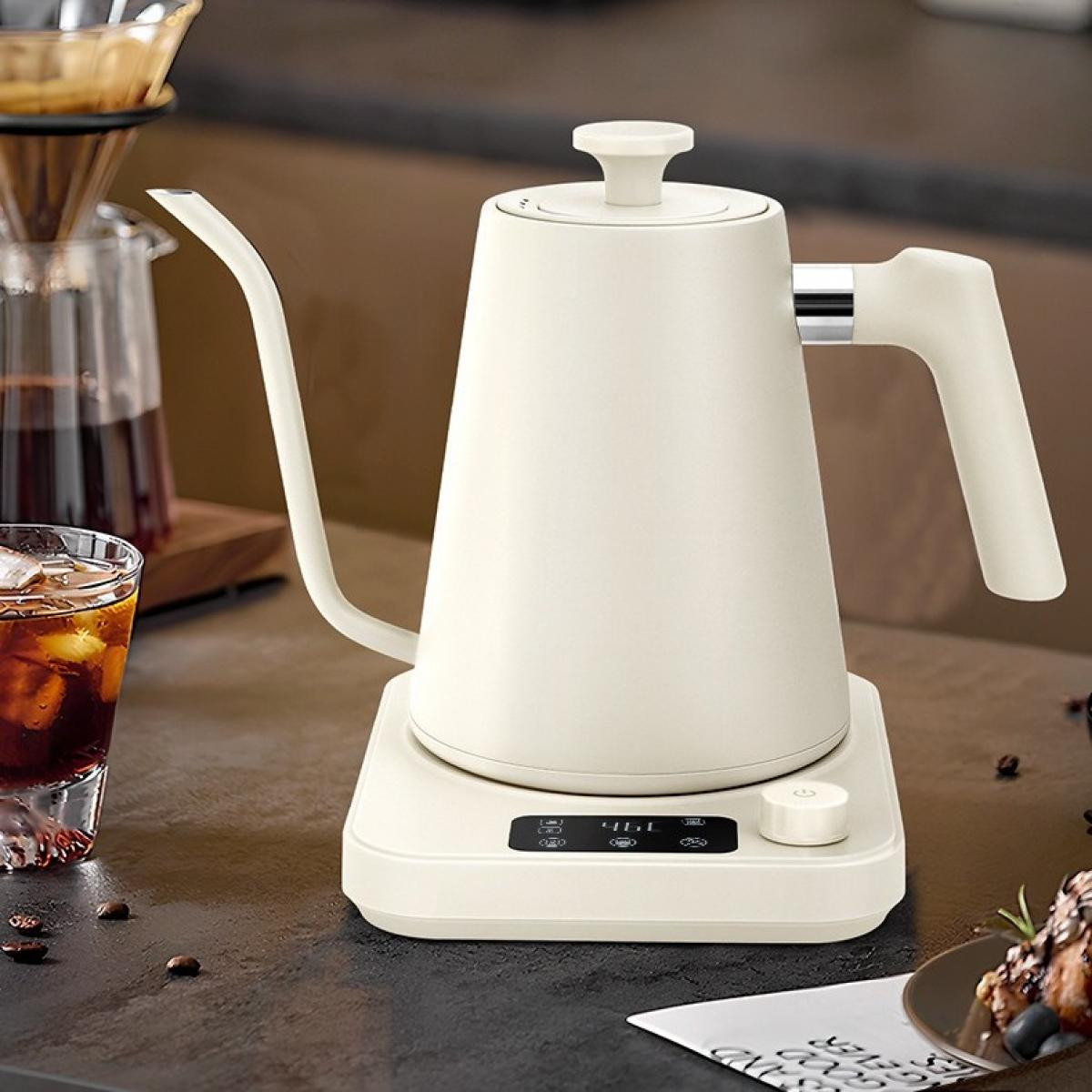 Cremefarbener Wasserkocher auf einem Ständer, Glas Eiskaffee, Kaffeemaschine und Kaffeebohnen auf dunkler Oberfläche.