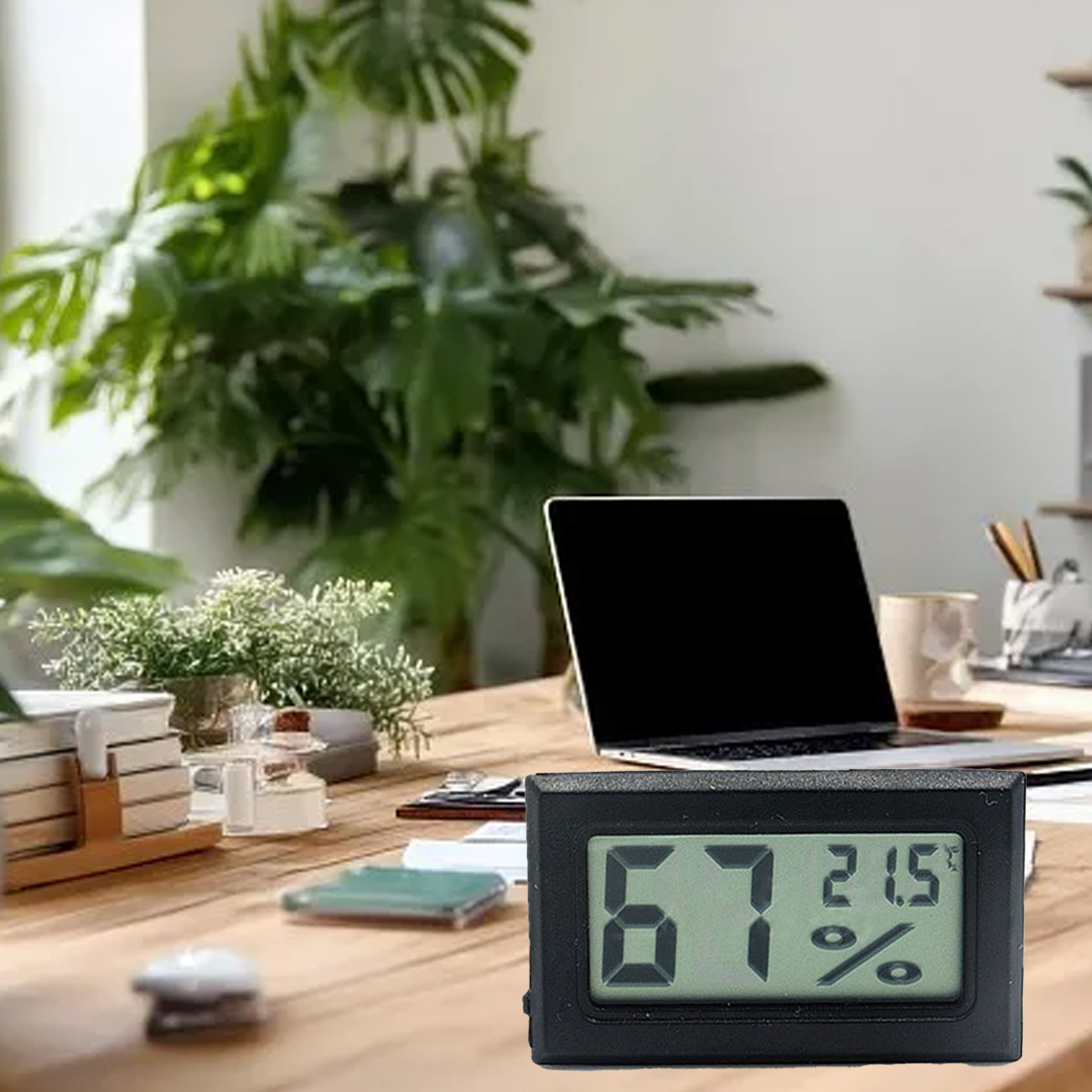 Ein Schreibtisch mit Laptop, Pflanzen und einem digitalen Hygrometer, das 67 % Luftfeuchtigkeit und 21,5 Grad anzeigt.