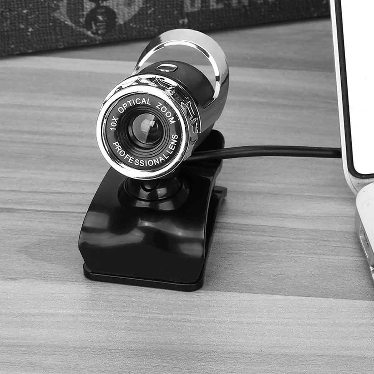 Eine Webcam mit schwarzem Sockel und silberner Linse steht auf einer Holzoberfläche. Das Objektiv ist mit '10X Optical Zoom Professional Lens' beschriftet.