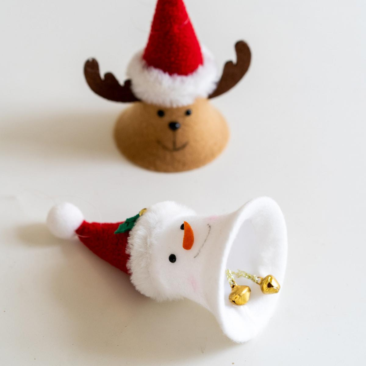 Weihnachtsschmuck: ein Rentierkopf und eine Schneemann-Glocke. Beide tragen Weihnachtsmützen, auf weißem Untergrund.