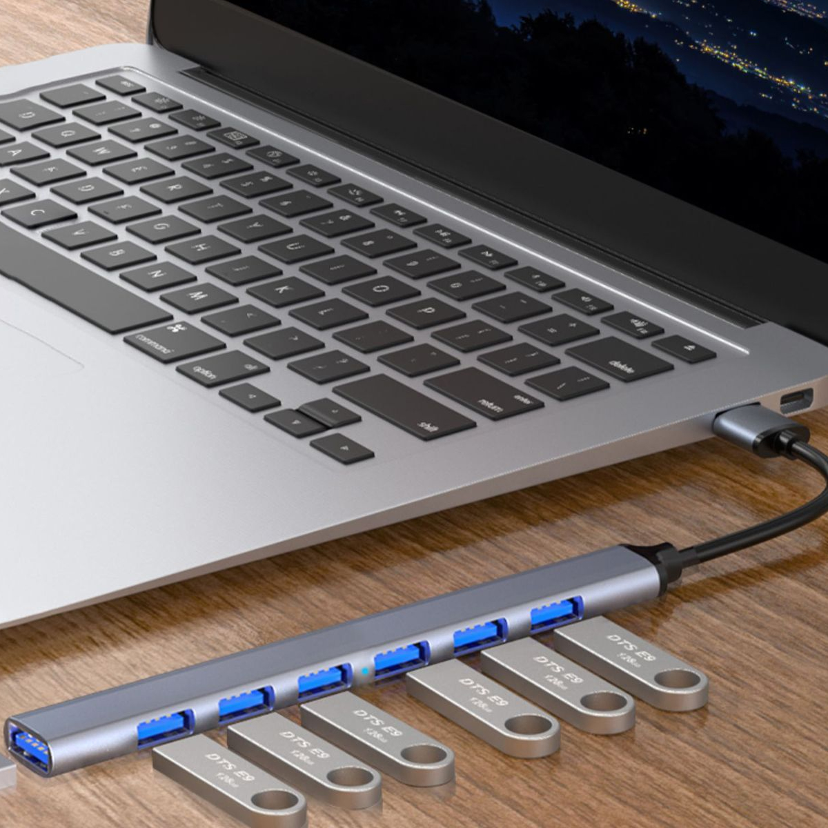 Laptop mit USB-Hub und Flash-Laufwerken auf einem Holztisch. Der Laptop-Bildschirm zeigt eine Nachtansicht.