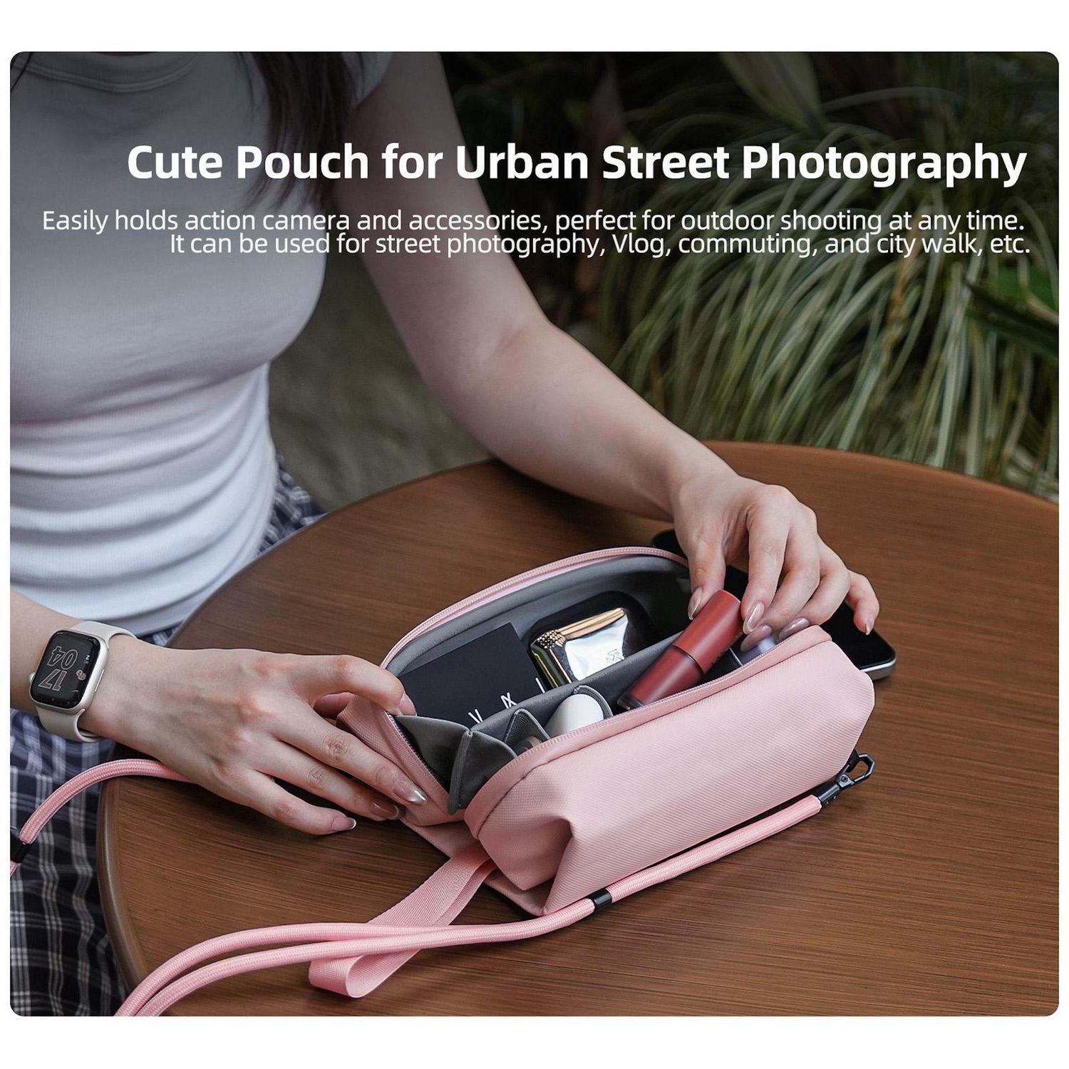 Eine Person hält eine rosa Tasche mit Zubehör auf einem Tisch. Die Tasche ist geöffnet und zeigt Gegenstände wie Lippenstift und ein Telefon.