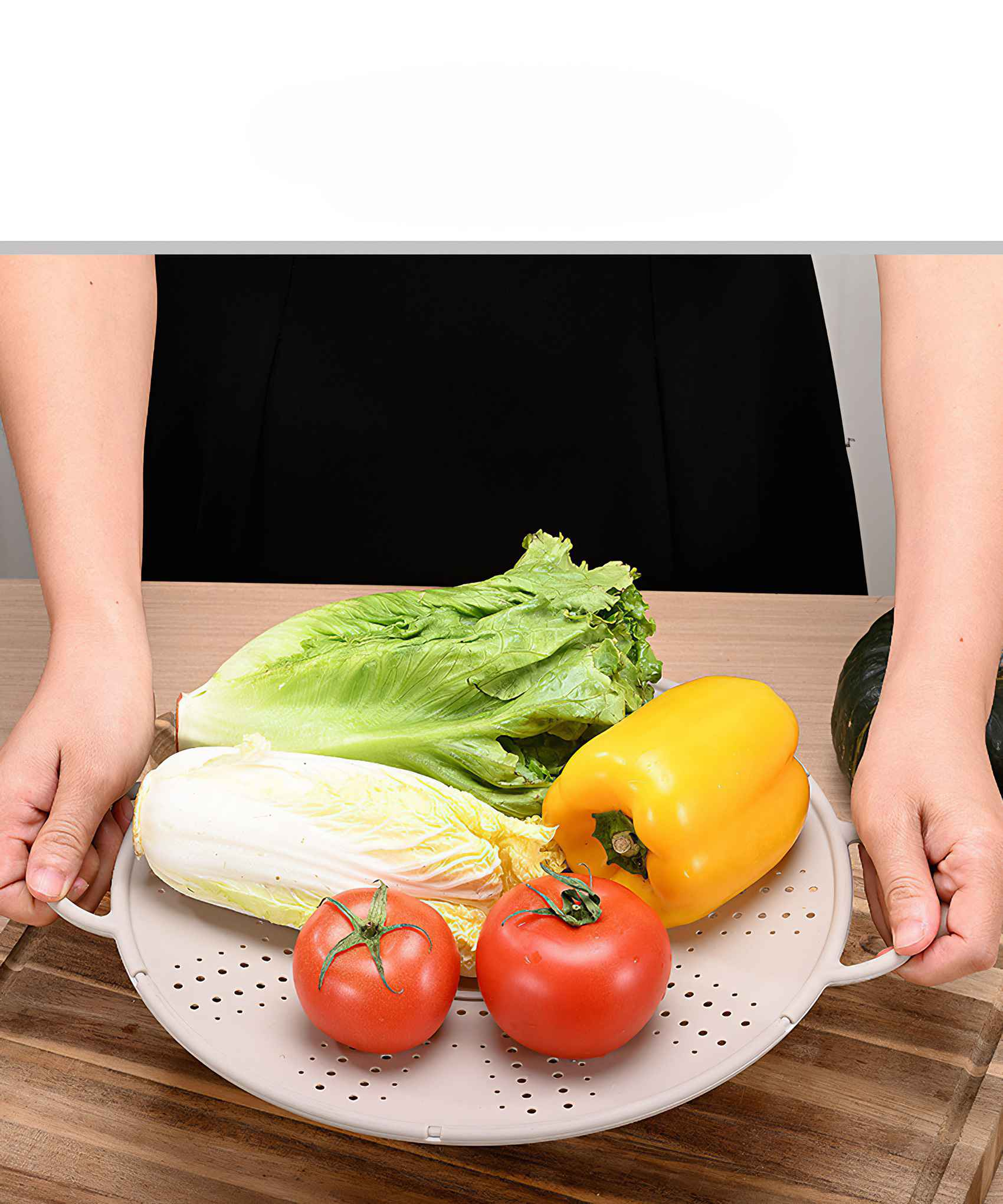 Eine Person, die ein Tablett mit Gemüse hält: Salat, Kohl, gelber Paprika und Tomaten. Der Hintergrund ist ein Holztisch.