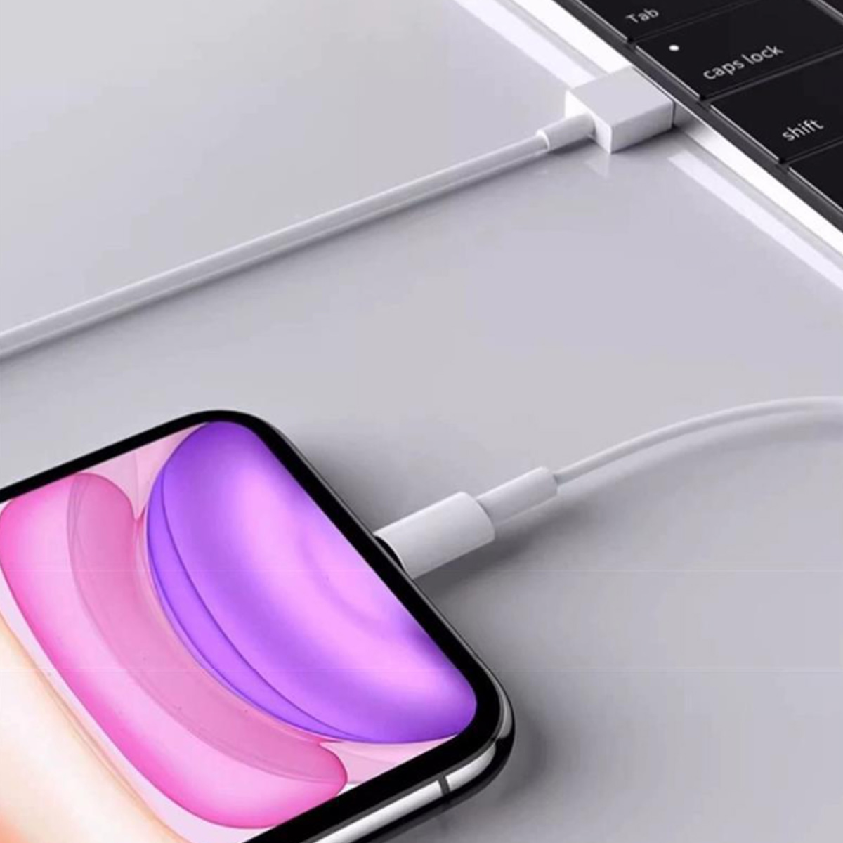 Ein weißes Ladekabel verbindet ein Smartphone mit einem lila-rosa Bildschirm mit einer Laptop-Tastatur.