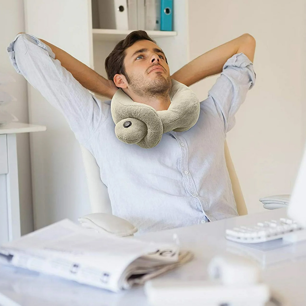 Mann im Bürostuhl mit Nackenkissen, Arme hinter dem Kopf, nach oben blickend. Schreibtisch mit Papier, Maus, Tastatur und Computer.