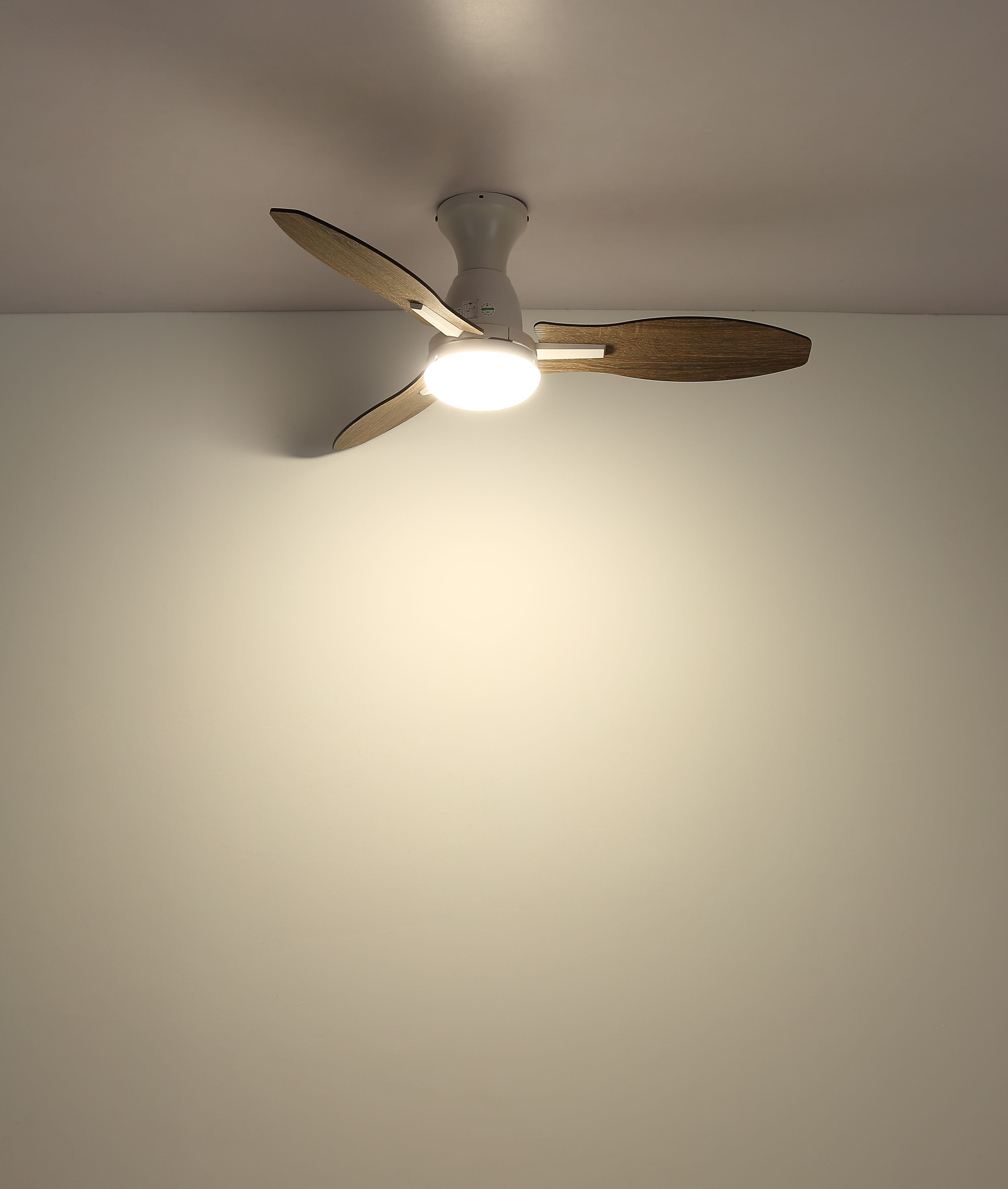 Ein Deckenventilator mit drei Holzblättern und einer zentralen Lichtvorrichtung ist an der Decke montiert.