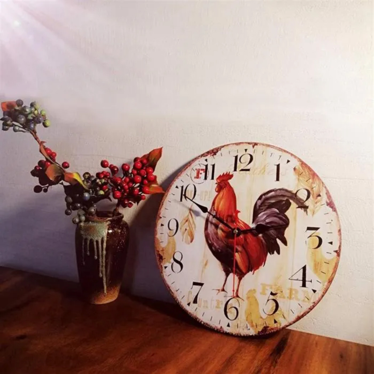Eine Kuckucksuhr steht auf einem Holztisch neben einer Vase mit Beeren und Blättern. Der Hintergrund ist eine weiße Wand.