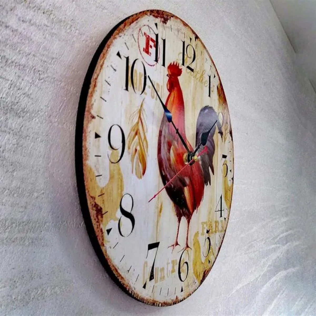Eine runde Uhr mit einem Hahn-Design. Sie hat schwarze Zeiger, große Zahlen und ein verblasstes, rustikales Aussehen. Die Uhr hängt an einer Wand.