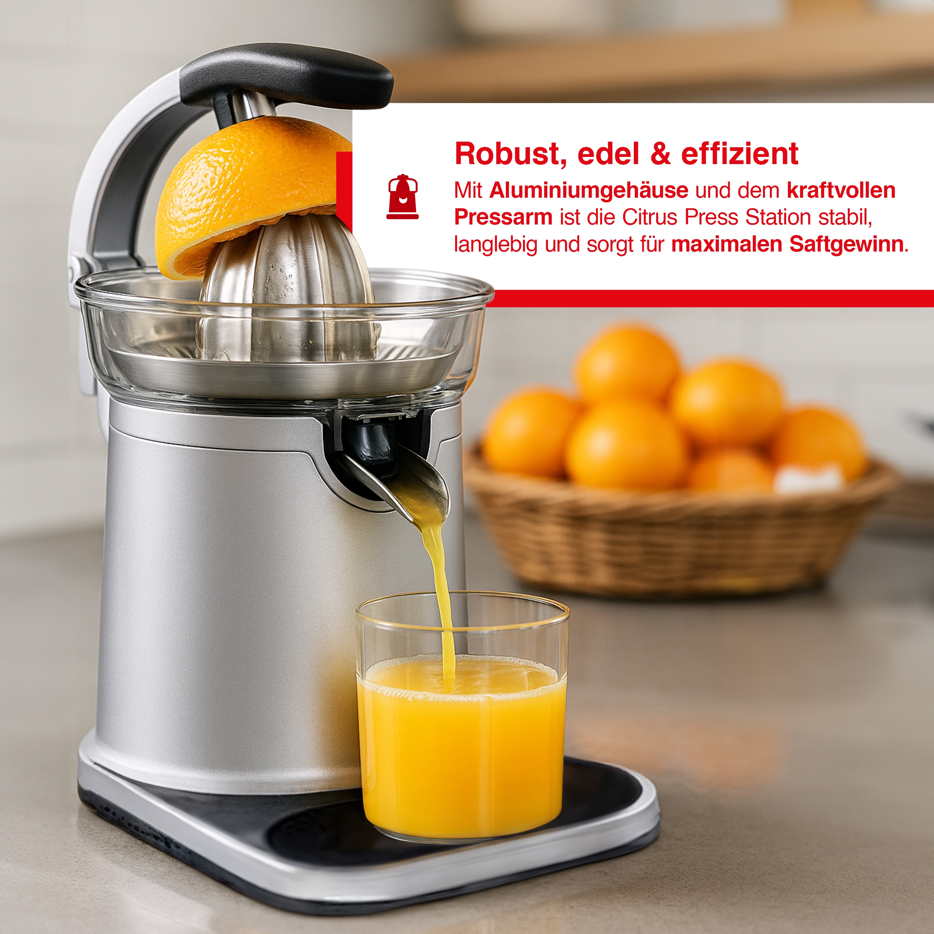 Ein Entsafter mit einer halben Orange obenauf, der frischen Saft in ein Glas gießt. Orangen sind in einem Korb im Hintergrund.