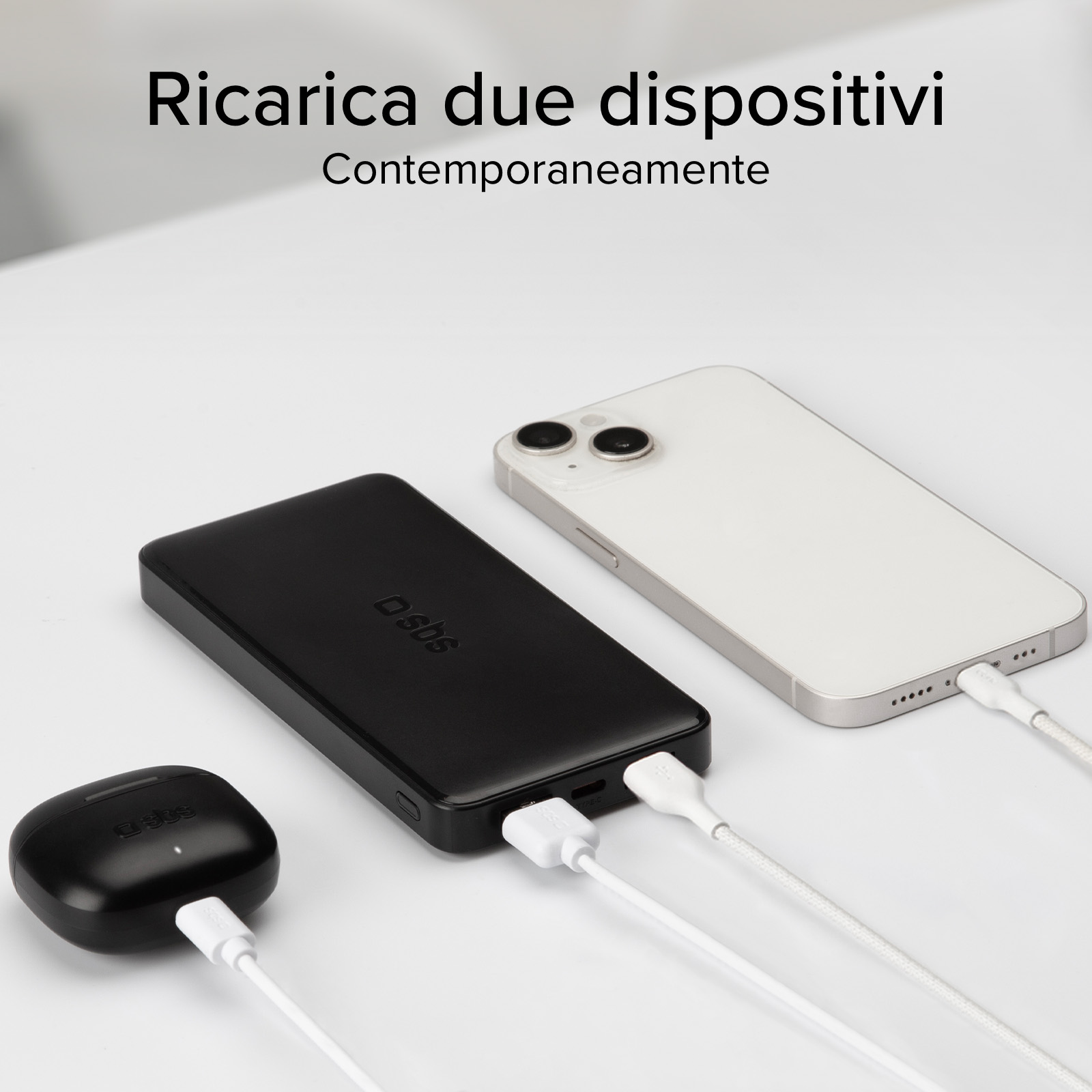 Un telefono bianco, un power bank nero e auricolari neri si ricaricano su una superficie bianca. I cavi collegano ogni dispositivo.