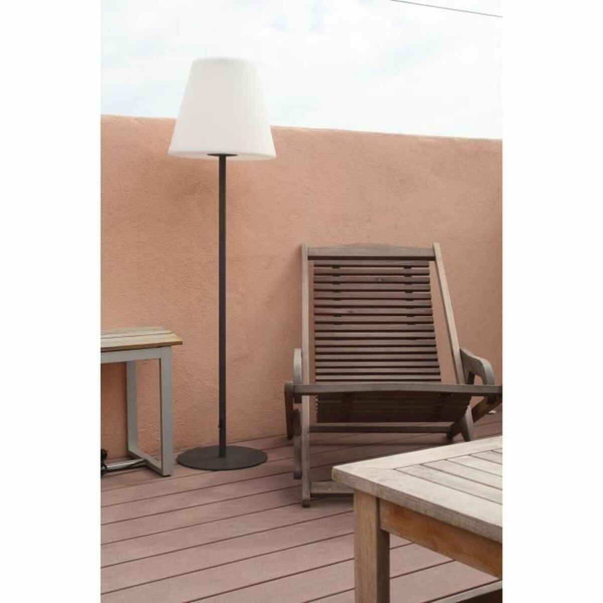 Eine Terrassenszene mit weißer Lampe, Holzstuhl und Tisch. Der Hintergrund ist eine pfirsichfarbene Wand und ein bewölkter Himmel.