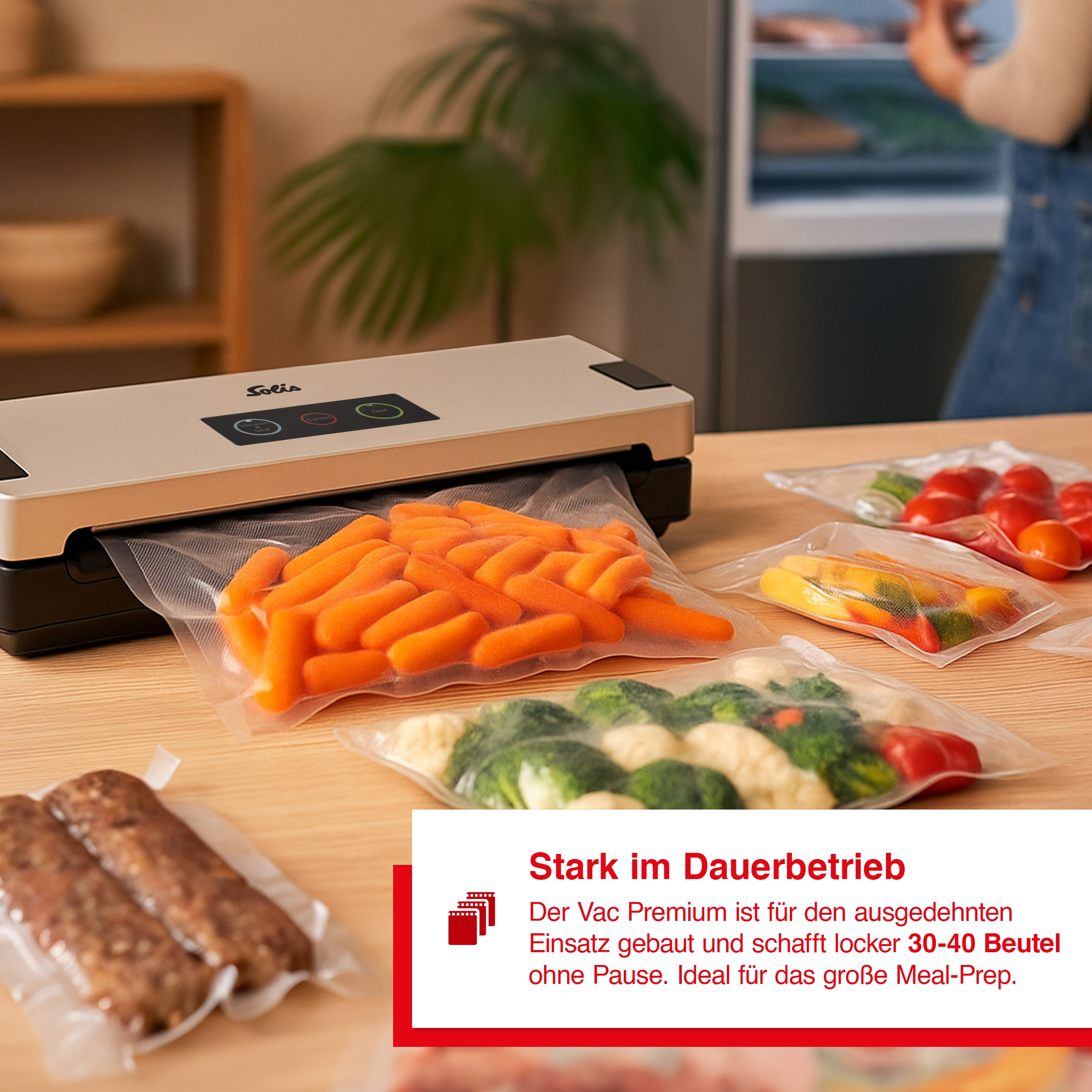 Vakuumiergerät mit Gemüse in Beuteln, darunter Karotten, Paprika und Brokkoli, auf einem Holztisch. Eine Person ist im Hintergrund.