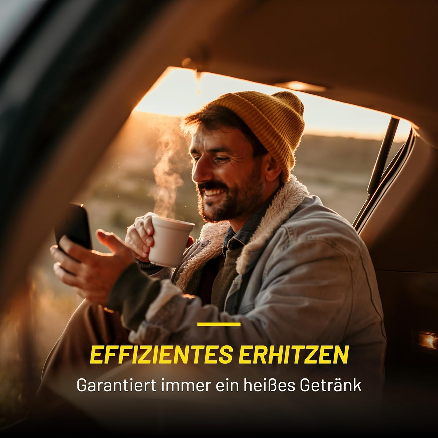 Mann in Mütze und Jacke sitzt im Auto, hält Handy und Kaffeetasse, lächelt. Im Hintergrund geht die Sonne unter.
