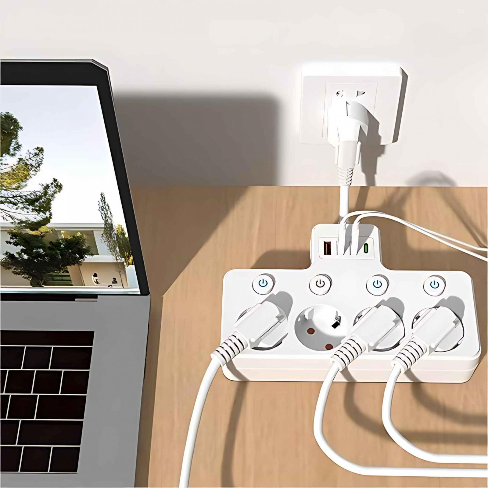 Ein Laptop, eine weiße Steckdosenleiste mit Steckern und eine Wandsteckdose befinden sich auf einer Holzoberfläche. Der Laptop zeigt Bäume und ein Haus.