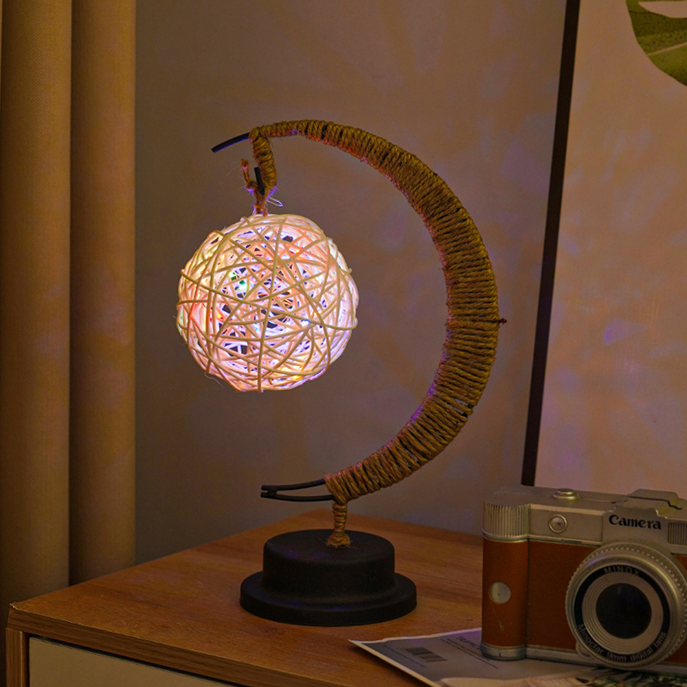 Eine dekorative Lampe in Mondform mit leuchtender Kugel. Eine Kamera steht auf einer Holzoberfläche.