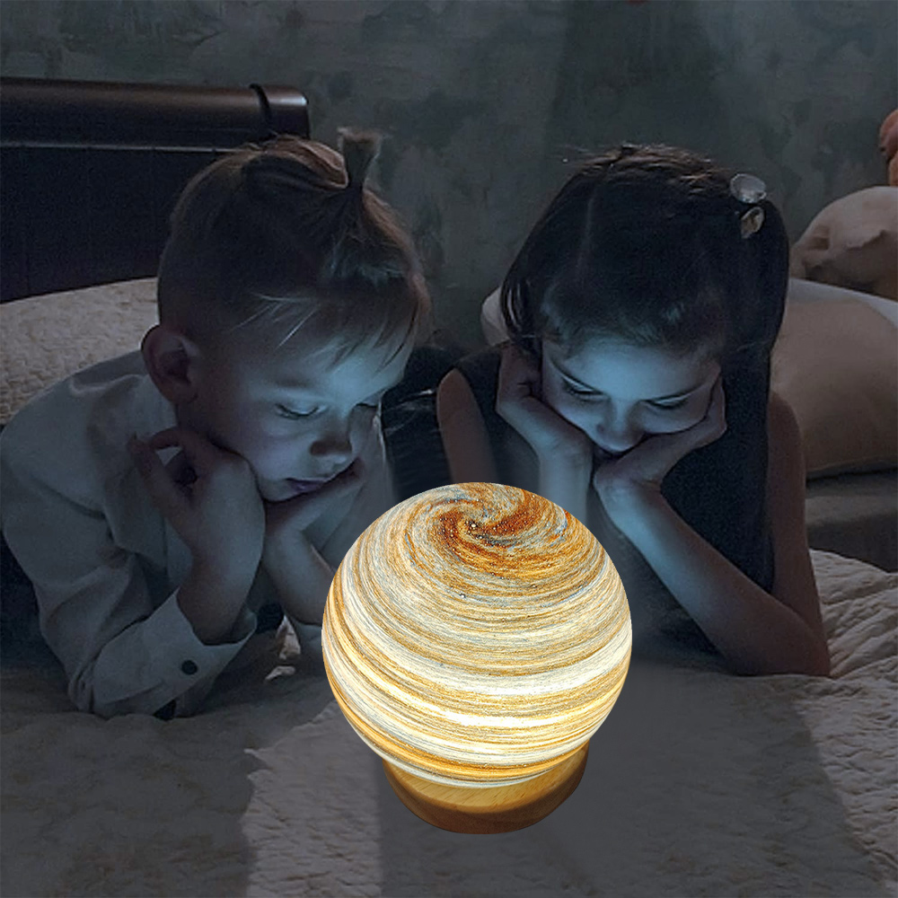 Zwei Kinder betrachten eine leuchtende, planetenförmige Lampe auf einem Bett. Die Lampe ist mit Braun und Weiß gestreift.