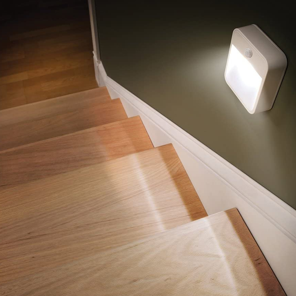 Holztreppe mit Wandleuchte. Das Licht ist eingeschaltet und beleuchtet die Stufen. Die Wand ist grün.