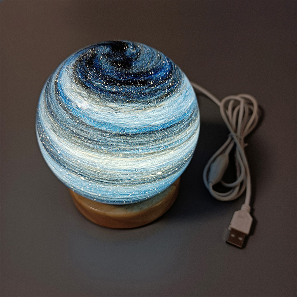 Ein kugelförmiges Nachtlicht mit Galaxiemotiv steht auf einem Holzsockel. Ein weißes USB-Kabel ist angeschlossen.