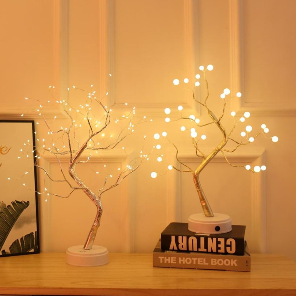 Zwei dekorative Baumlampen mit leuchtenden Lichtern stehen auf einer Holzoberfläche. Ein Buch mit 'CENTURY' ist darunter.