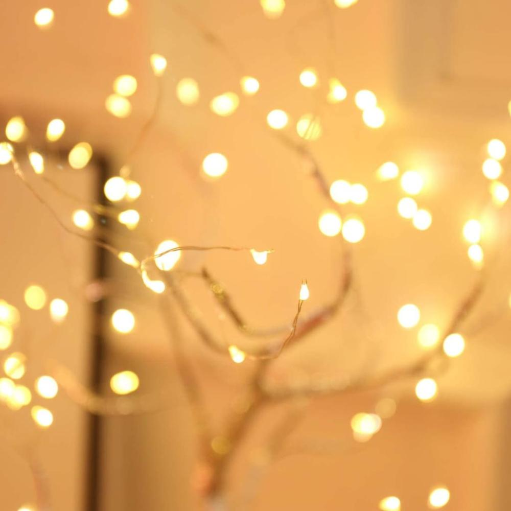 Warme, leuchtende Lichter an dünnen Drähten, die einem kleinen Baum ähneln. Weicher Fokus mit goldenem Hintergrund, gemütliche, festliche Atmosphäre.