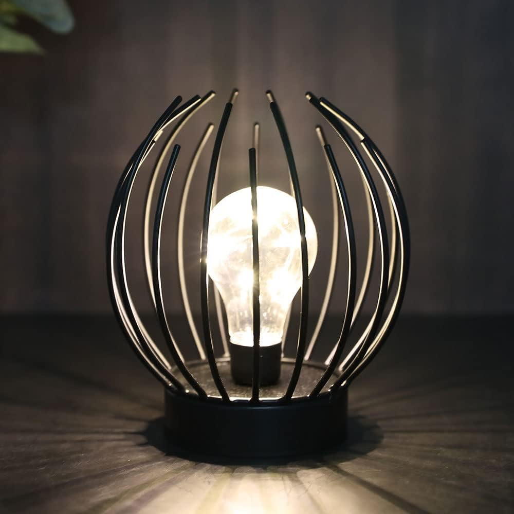 Eine dekorative Lampe mit einer leuchtenden Glühbirne in einem schwarzen Metallkäfig. Der Hintergrund ist dunkel.