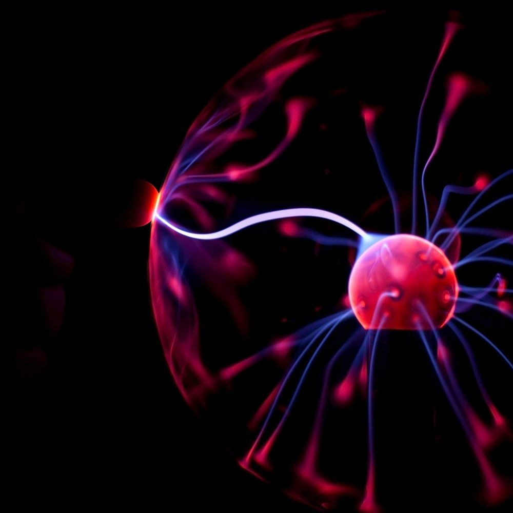 Eine Plasmakugel leuchtet rot und blau. Elektrizitätsbögen gehen von einer zentralen Kugel aus, vor schwarzem Hintergrund.