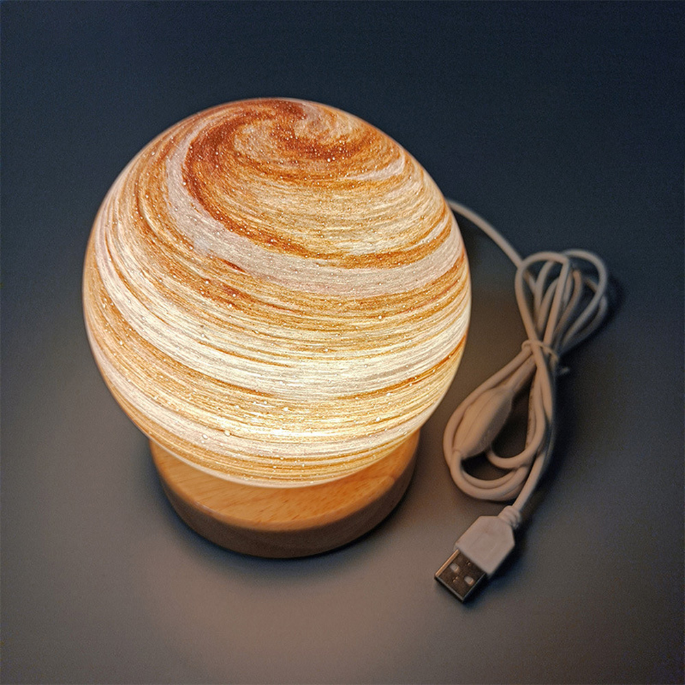 Eine kugelförmige Lampe mit einem Wirbelmuster aus Braun und Weiß. Sie steht auf einem Holzsockel mit einem USB-Kabel. Der Hintergrund ist grau.