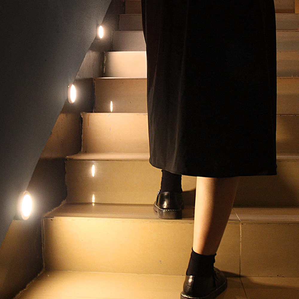 Eine Person in schwarzem Kleid und Schuhen geht eine Treppe hinauf. Lichter sind an der Wand. Die Treppe ist beleuchtet.