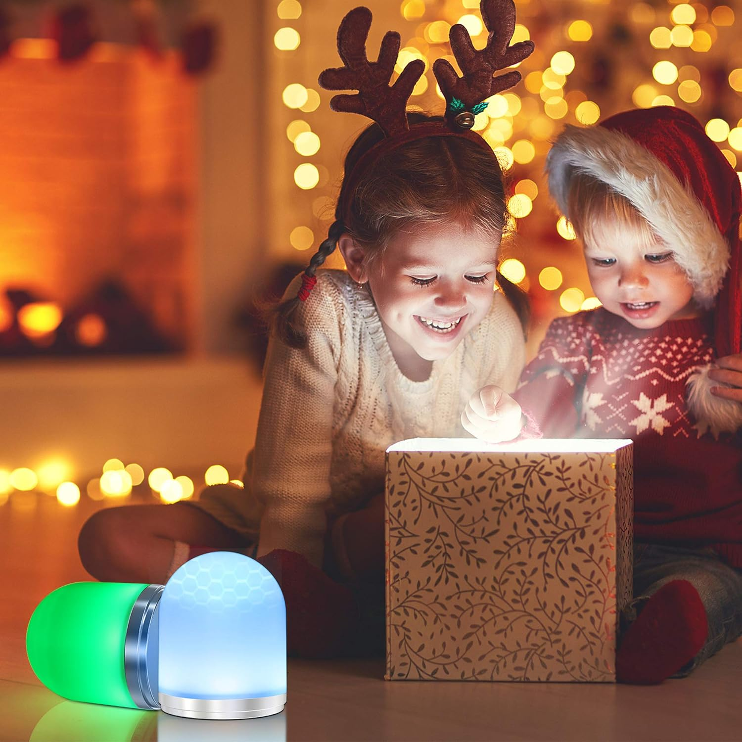 Zwei Kinder öffnen eine leuchtende Geschenkbox. Ein Mädchen mit Geweih und ein Junge mit Weihnachtsmütze. Zwei Lampen davor.