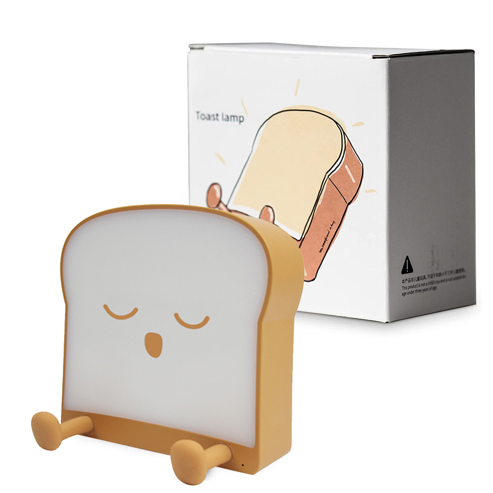 Eine toastförmige Lampe mit geschlossenen Augen und einem lächelnden Mund. Eine Schachtel mit einem Toastbild und dem Text 'Toastlampe' befindet sich dahinter.