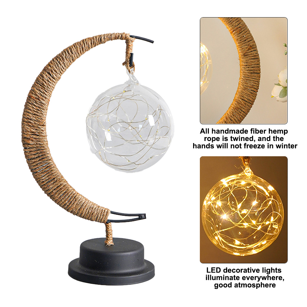 Eine dekorative Lampe mit einem hanfummantelten Halbmond und einer Glaskugel mit Feenlichtern auf schwarzem Sockel.