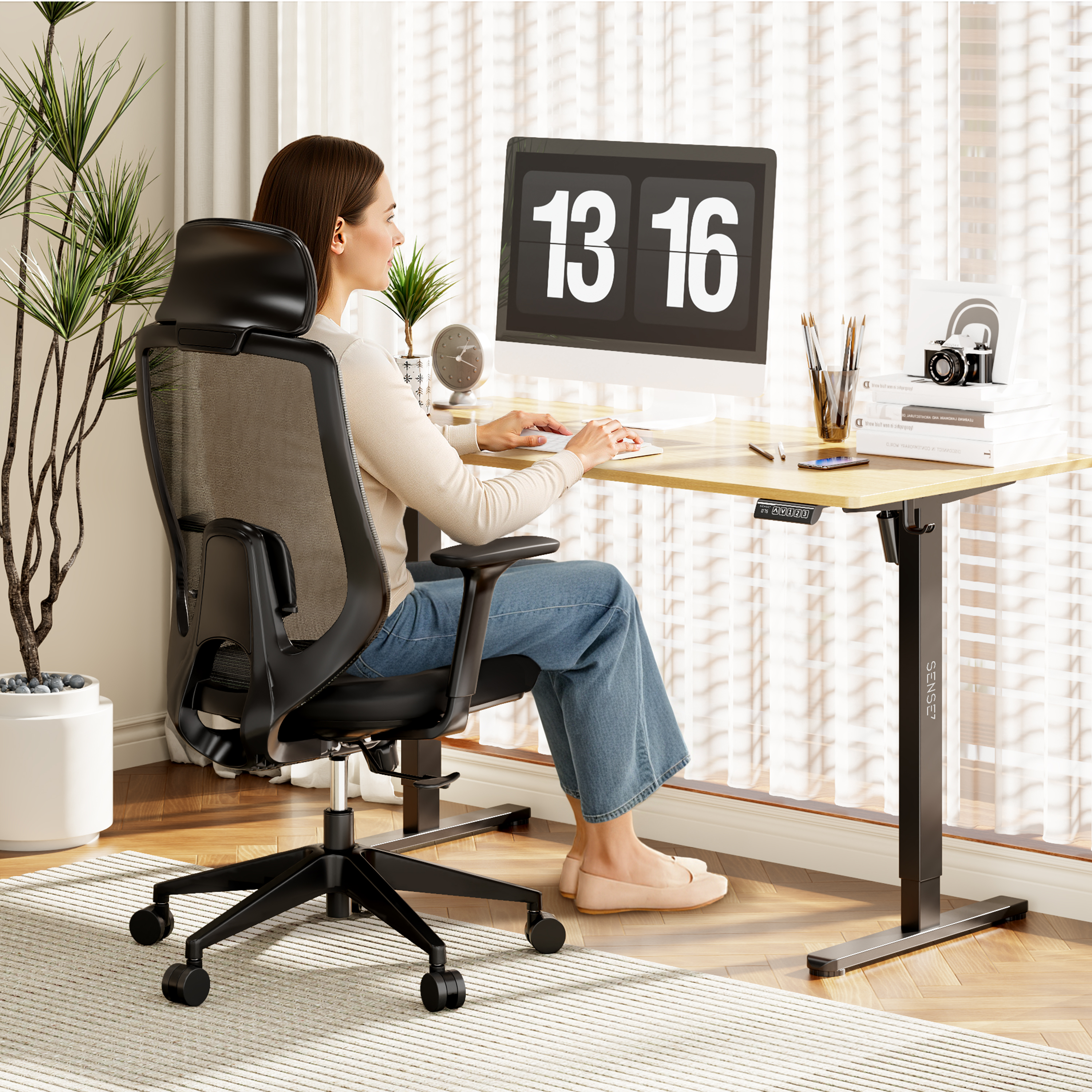 Eine Frau sitzt am Schreibtisch und tippt. Ein Computermonitor zeigt 13:16. Ein schwarzer Bürostuhl und eine Pflanze sind ebenfalls zu sehen.