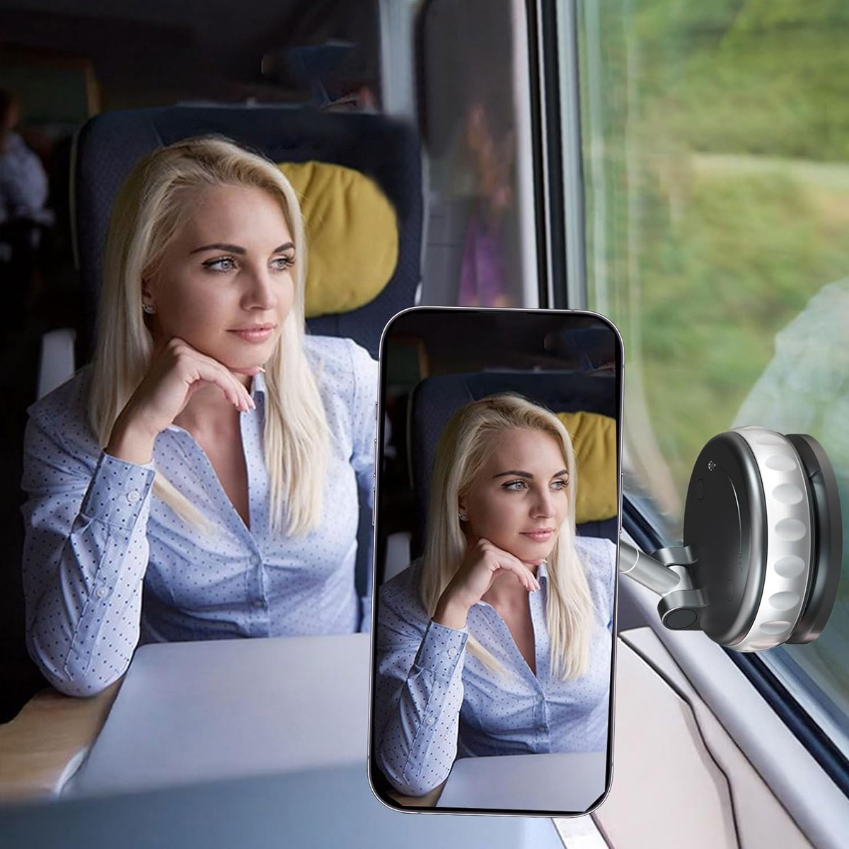 Blonde Frau im Zug, blickt aus dem Fenster. Ein Telefon zeigt das gleiche Bild. Ein Gerät ist am Fenster befestigt.