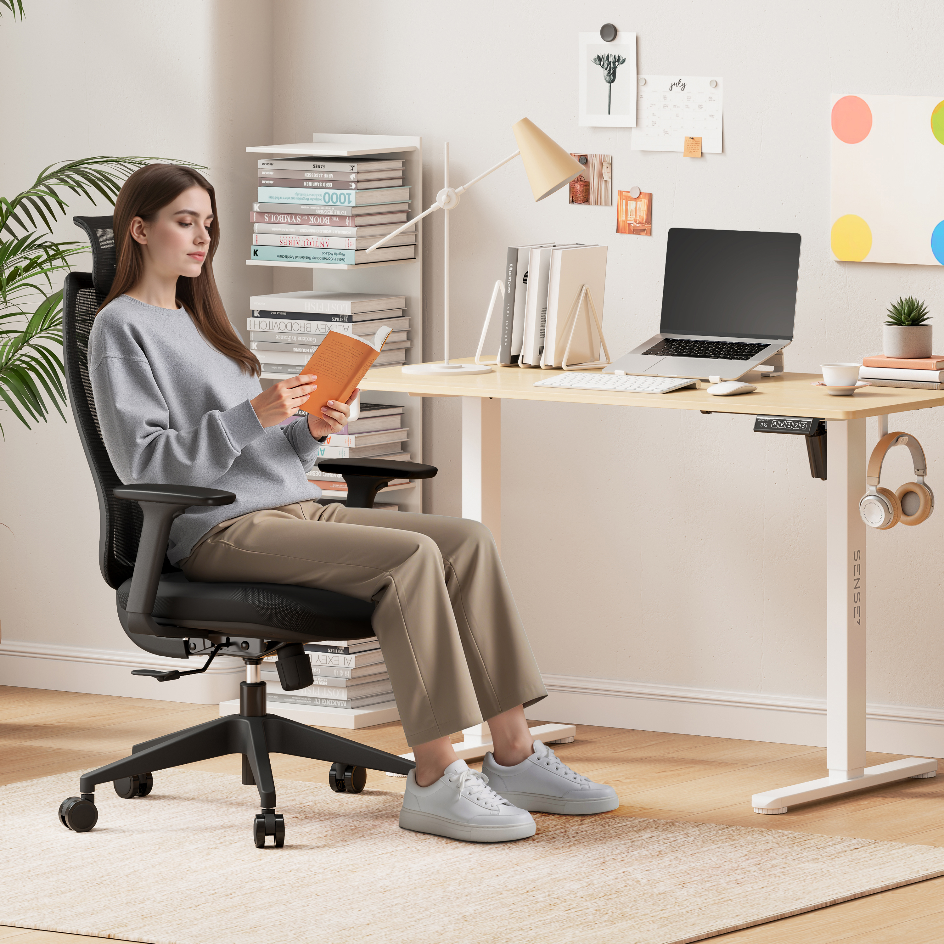 Una donna legge su una sedia a una scrivania con un laptop. Sono presenti anche libri, una lampada e cuffie.