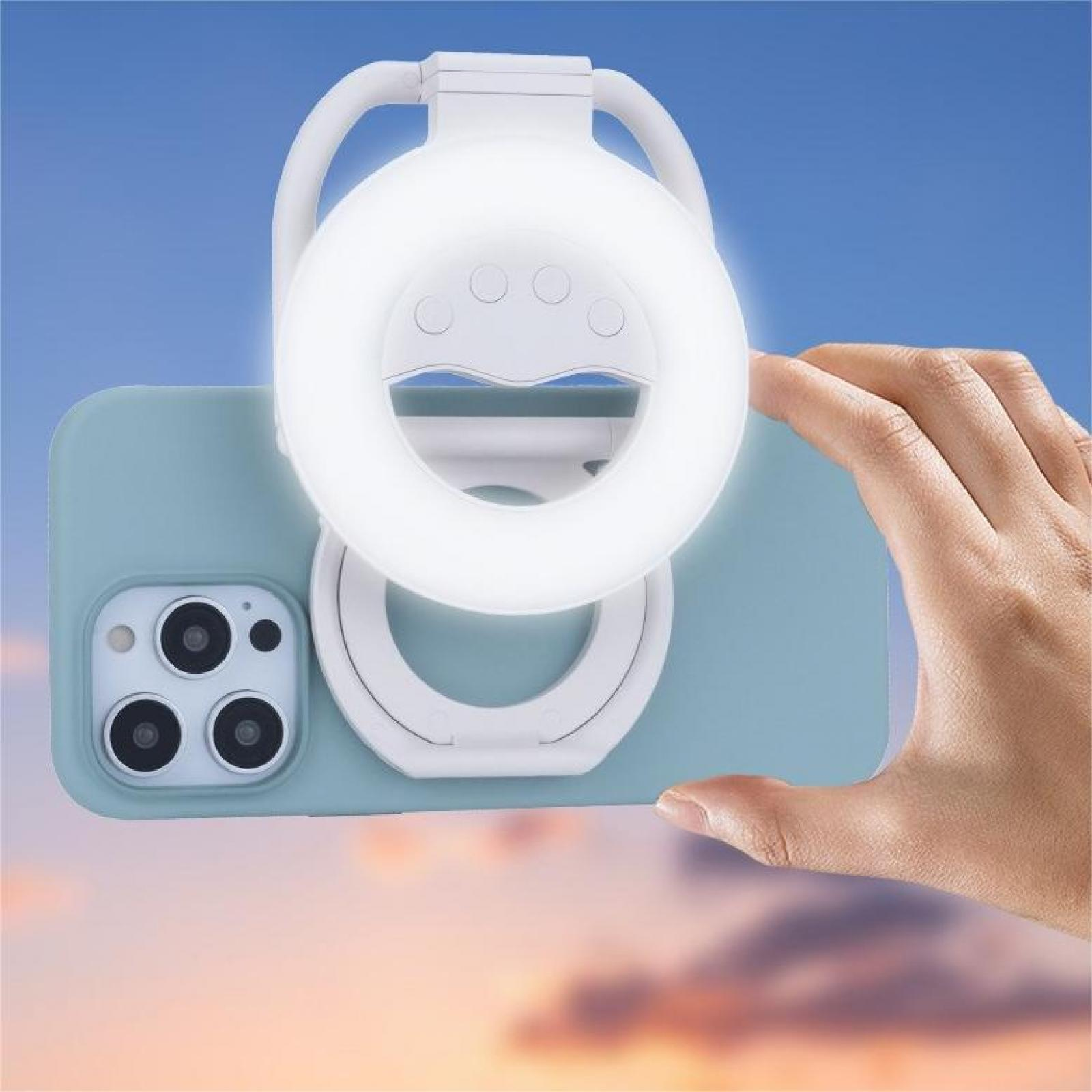 Ein Ringlicht ist an einem Telefon befestigt. Eine Hand hält das Telefon, der Hintergrund ist ein Farbverlauf aus Blau und Orange.