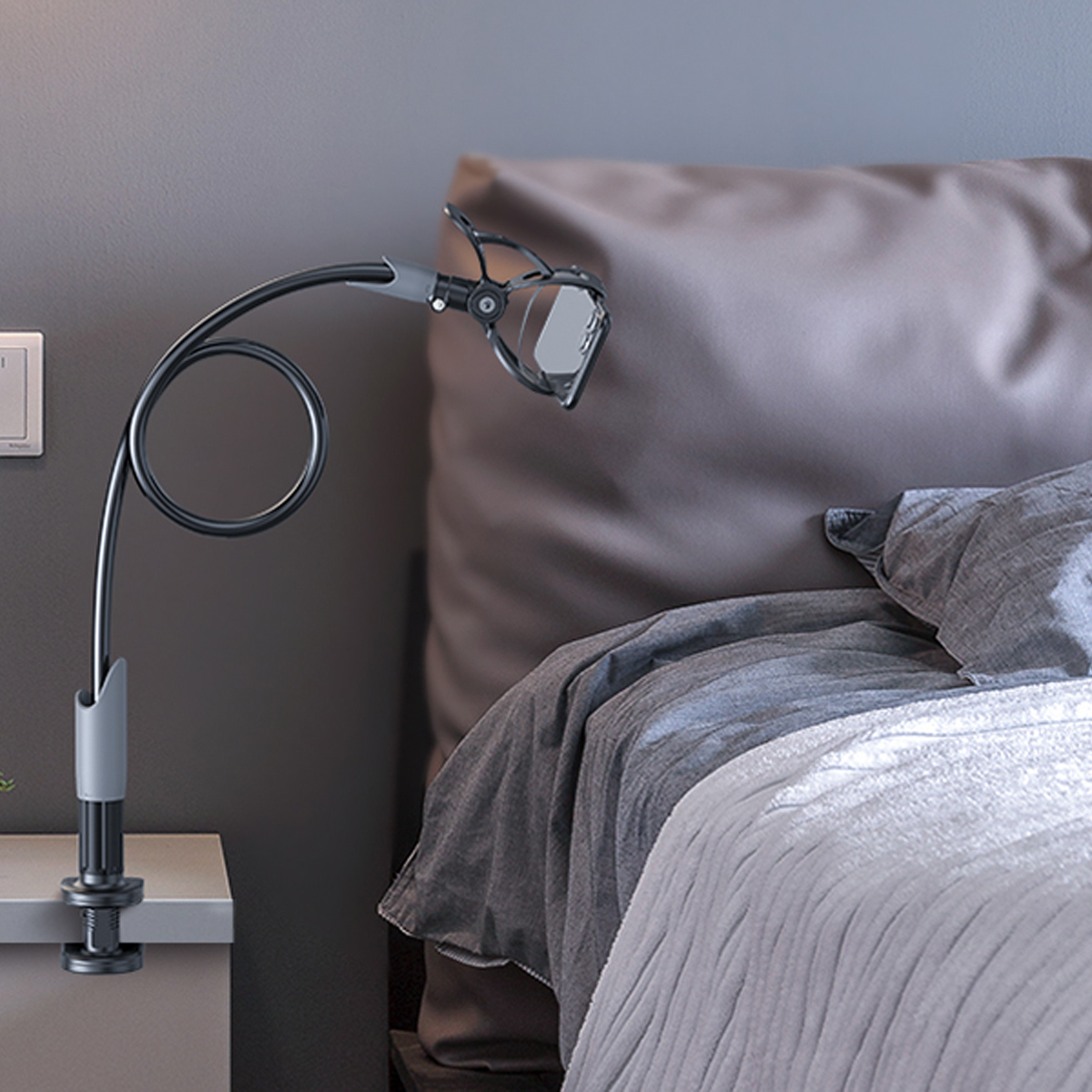 Ein Telefonhalter, der an einem Nachttisch befestigt ist, ein gebogener Arm, der eine Telefonklemme hält. Bett mit Kissen und Decke im Hintergrund.