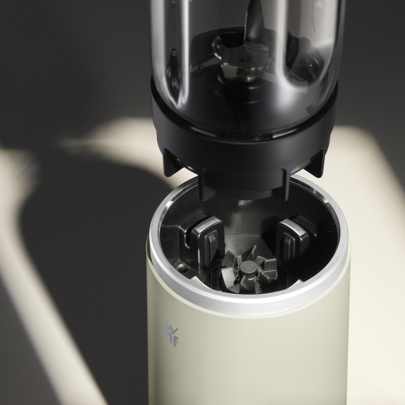 Nahaufnahme eines zerlegten Mixers. Die Mixerbasis ist hellgrün. Der Klingelbehälter ist schwarz und transparent.