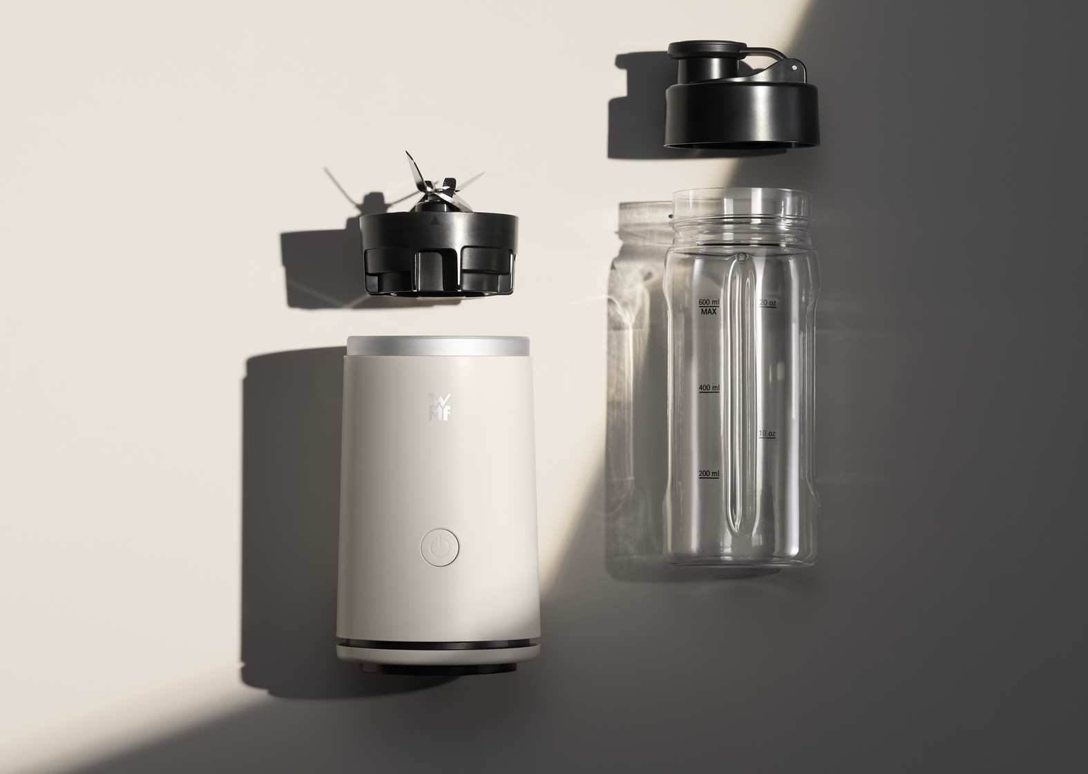 Blenderteile: Sockel, Klinge, Flasche und Deckel. Beigefarbener Sockel, schwarze Klinge und Deckel, transparente Flasche. Alle Teile sind getrennt.