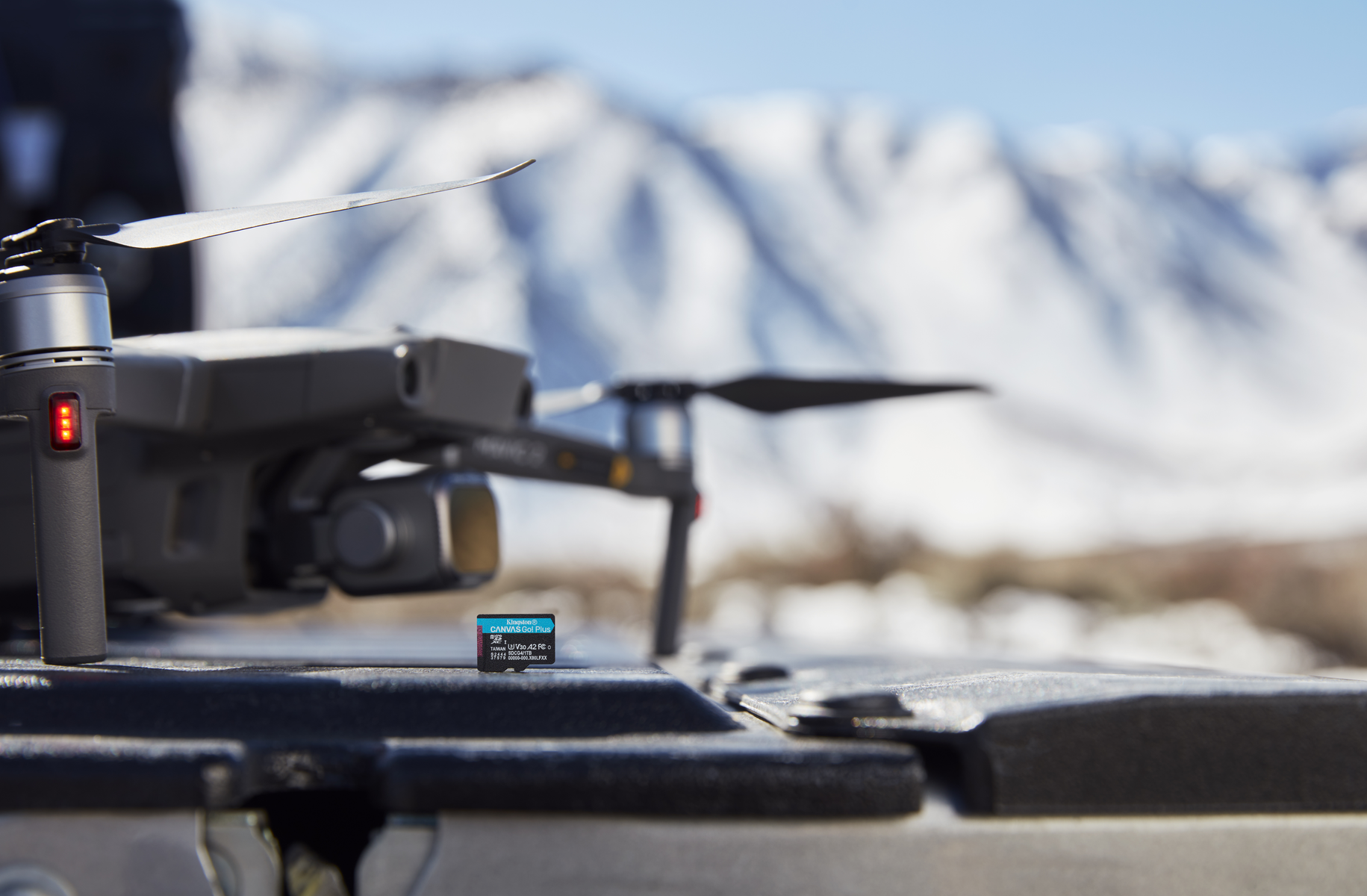 Dron z śmigłami i kartą pamięci na powierzchni. W tle góry ze śniegiem, pod błękitnym niebem.