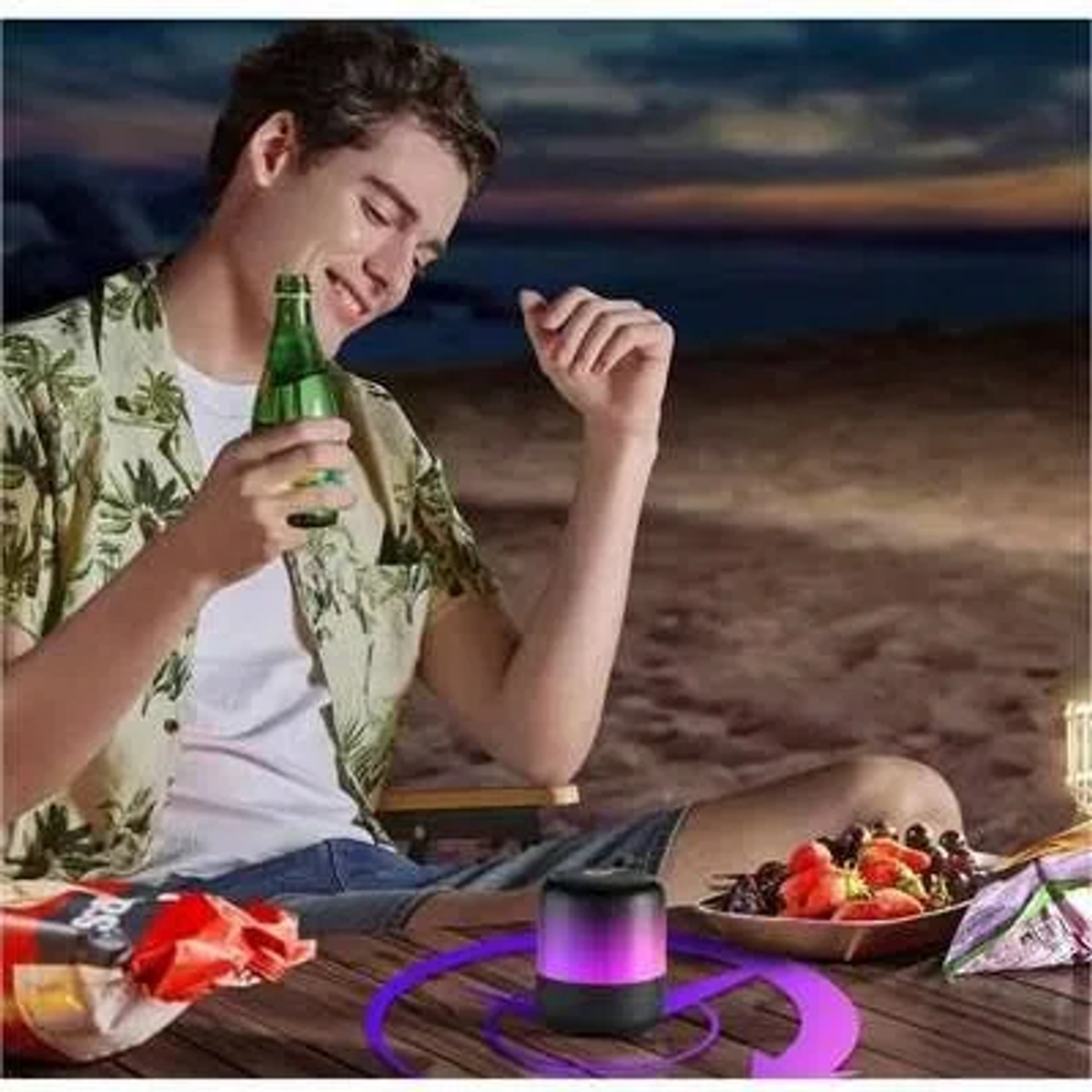 Mężczyzna trzyma zieloną butelkę, uśmiechając się. Głośnik, owoce i przekąski na stole. Plaża i zachód słońca w tle.