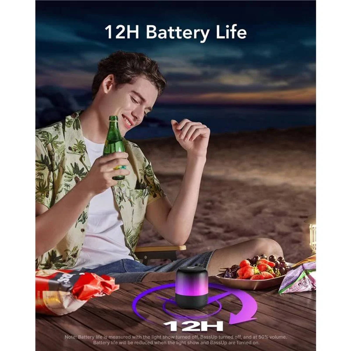 Mężczyzna trzyma butelkę, siedząc przy stole z głośnikiem, przekąskami i owocami. Tekst: 12H Żywotność baterii.