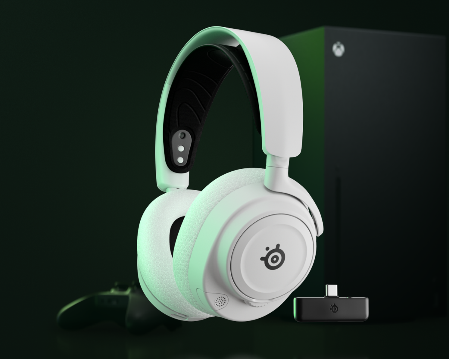 Cuffie da gaming bianche con dettagli neri, console Xbox, controller e un ricevitore nero su superficie illuminata di verde.
