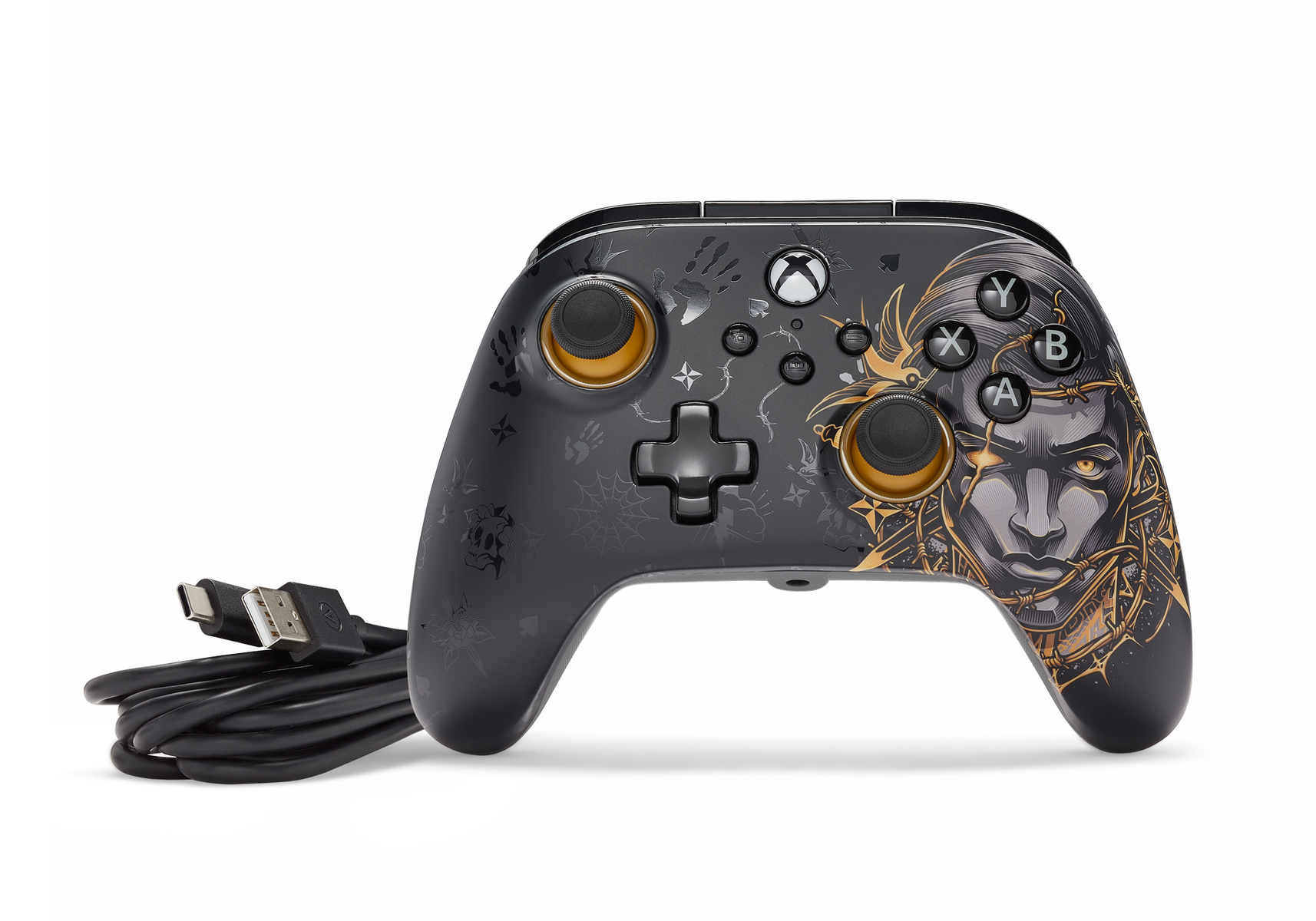 Czarny kontroler Xbox ze złotymi akcentami i wzorem twarzy. Ma czarny kabel i leży na białej powierzchni.