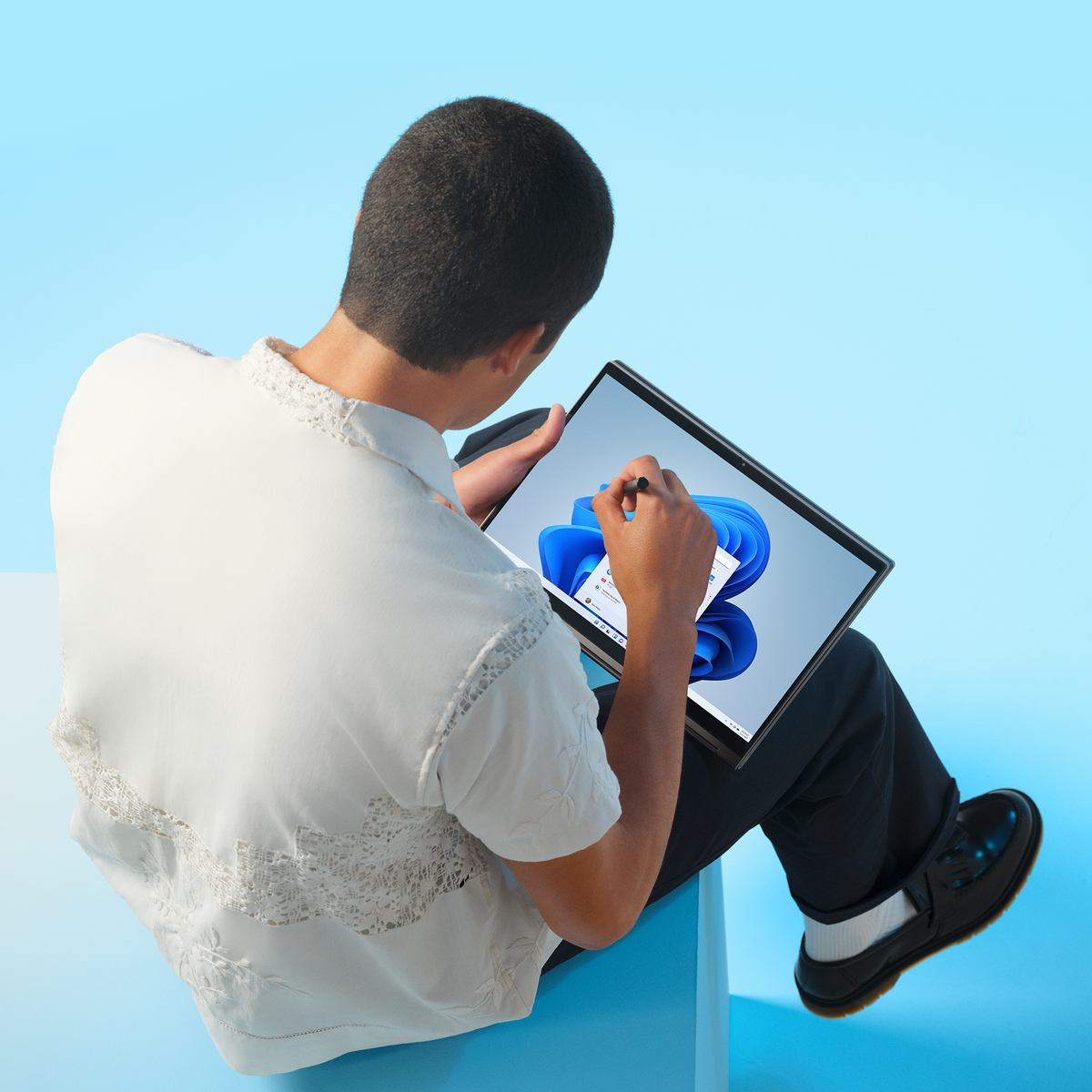 Osoba korzysta z tabletu z rysikiem, ekran pokazuje interfejs Windows 11. Osoba ma na sobie białą koszulę. Niebieskie tło.