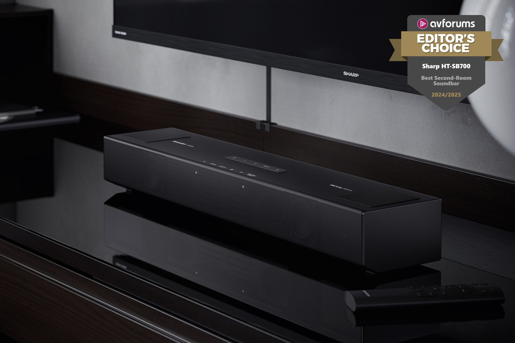 Czarny soundbar Sharp na odblaskowej powierzchni, pod TV. Odznaka: Editor's Choice. Pilot z przodu.