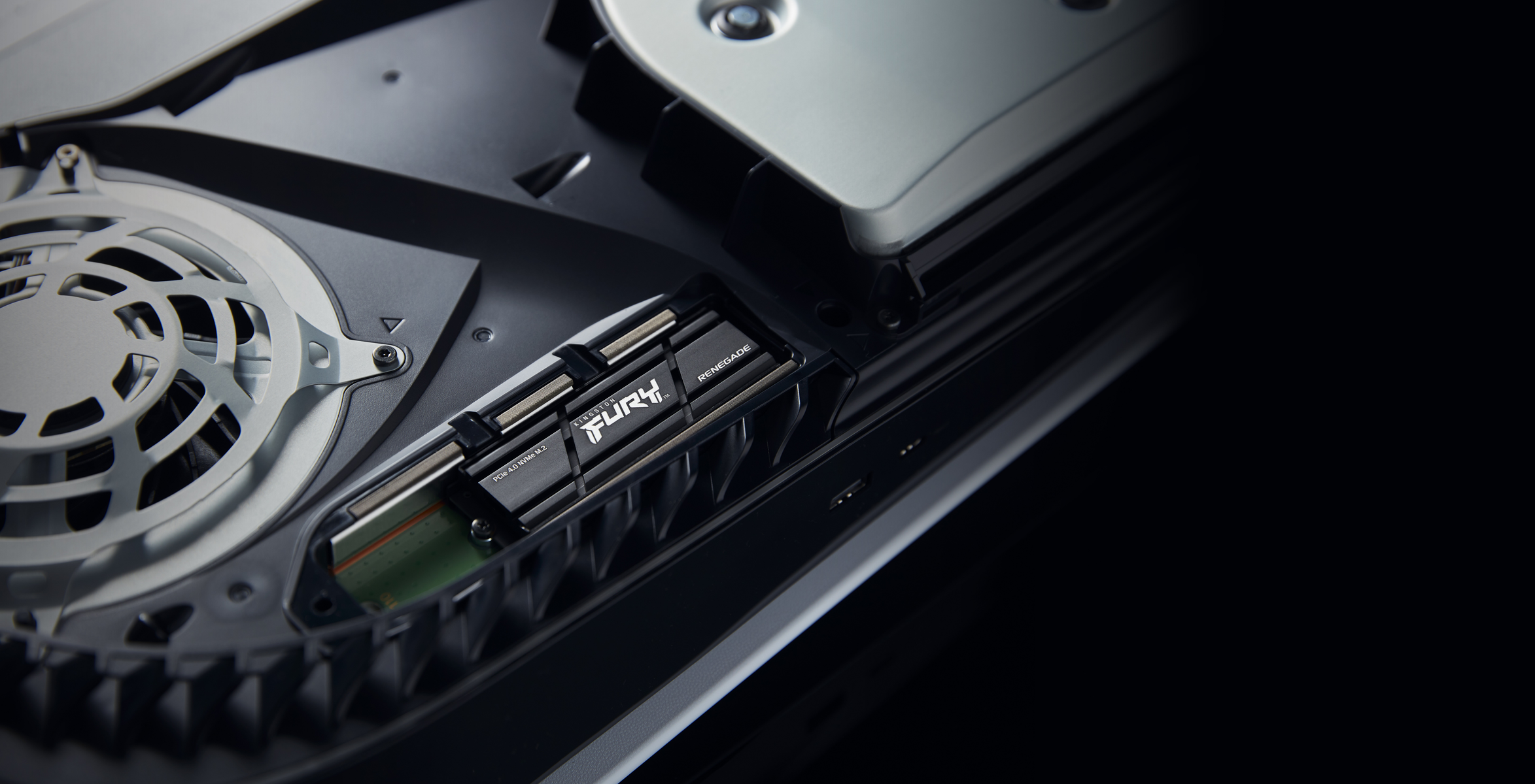 Zbliżenie wnętrza PS5 z dyskiem SSD Kingston FURY Renegade. Widoczny srebrny wentylator i czarne elementy.