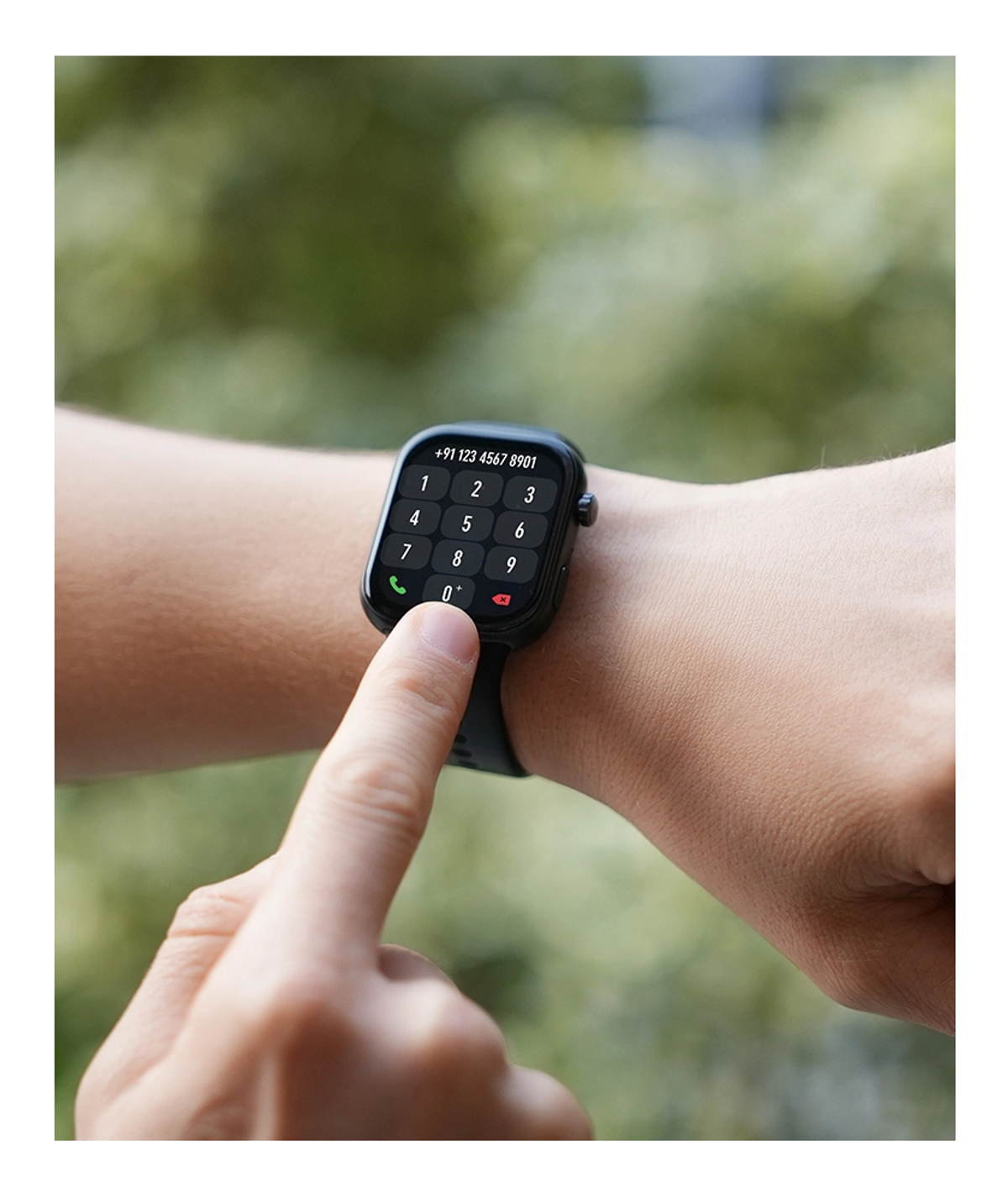 A person's wrist with a smartwatch displaying a dial pad. A finger presses the '0' button, dialing a number. Green background.