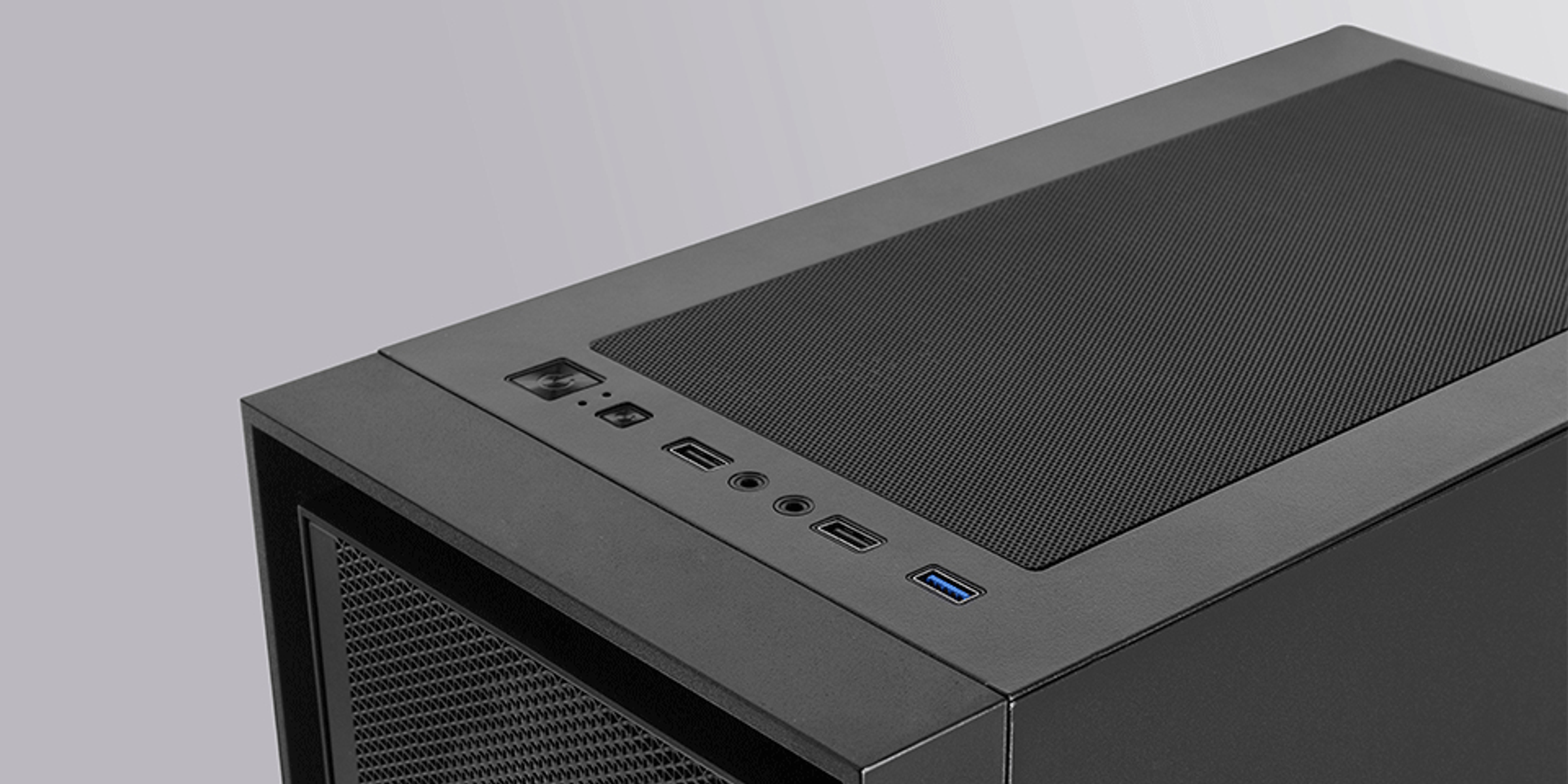 Zbliżenie czarnej obudowy komputera. Ma siatkowy wierzch, porty zasilania i USB. Tło jest szare.